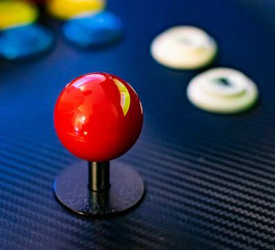 Red joystick and colorful buttons of vintage arcade game console. Close up view of old game control panel. Red sphere, ball. 