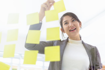 Young smiling asian business woman mentor leader write tasks creative ideas on sticky post it notes...