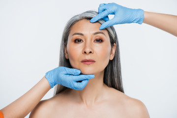 Fototapeta premium doctors in latex gloves touching face of naked asian woman with grey hair isolated on grey