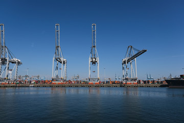 Obraz premium Huge cranes and ships anchored at harbor. International commercial port, city of Rotterdam background. Logistics business
