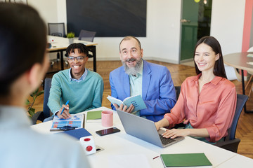 Group of modern business people in positive mood having meeting in office room, high angle over-the-shoulder shot