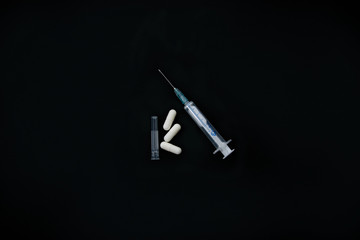 syringe and pills on black background