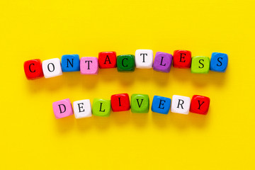 Contactless delivery inscription made with colorful wooden cubes over yellow background. On line shopping.