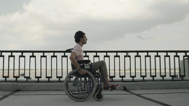 Man with paralysis of legs muscles is sitting in invalid carriage and riding. Ride from Right to Left