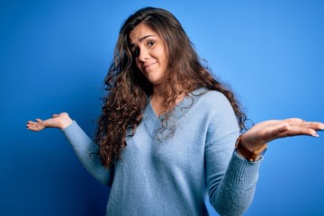 Young beautiful woman with curly hair wearing blue casual sweater over isolated background clueless...