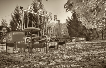 Fototapeta premium Kharkiv Park of Culture and Rest. Retro swing for children. Horizontal frame. Black and white photography, sepia. Photographed in Ukraine.
