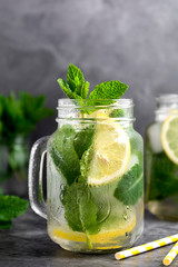 Glass mason jar of ice tea with fresh mint, lemon and paper straw on dark background. Summer healthy cold drink. Alternative medicine.