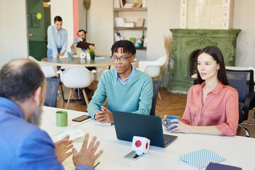 Group of three modern business people sitting together at office table discussing important issues