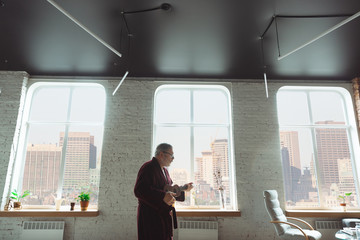 Playing on ukulele, guitar. Senior man during quarantine, realizing how important stay at home during virus outbreak. Concept of lockdown of coronavirus, self-insulation, healthcare, safety