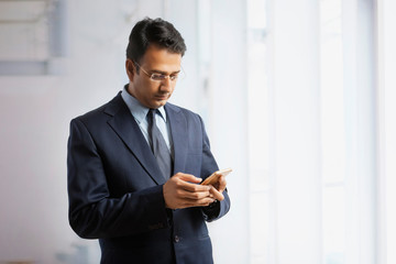 Businessman in formal clothes and eyeglasses standing in office using mobile phone
