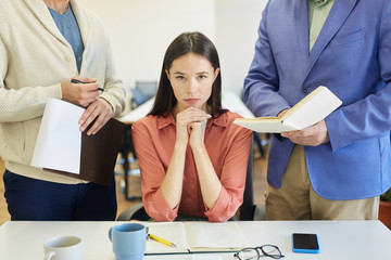 Angry young Caucasian woman sitting at office desk feeling stressed out at work, unrecognizable colleague and boss annoying her