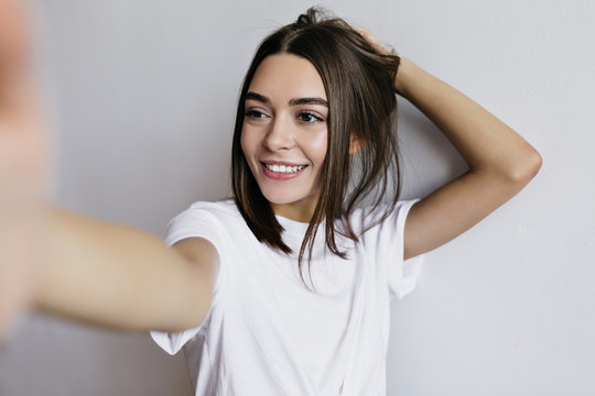 Beautiful tanned woman with brown eyes making selfie and laughing. Studio shot of elegant lady isolated on light background.