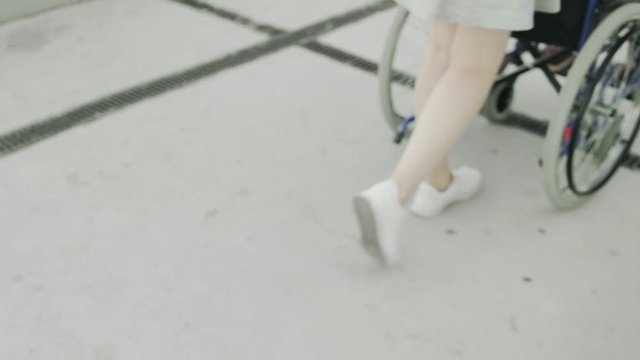 Woman is rolling invalid carriage with young man outdoors, close-up of legs