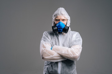 Fototapeta na wymiar Serious epidemiologist medical worker in protective coveralls, glasses and respirator holding hands crossed on chest. Concept of Coronavirus COVID-19 Pandemic. Studio shot on isolated dark background.