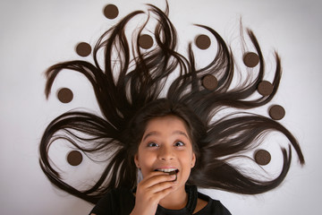 Close up of smiling girl lying on floor eating biscuit with her hair arranged in a tree design with biscuits
