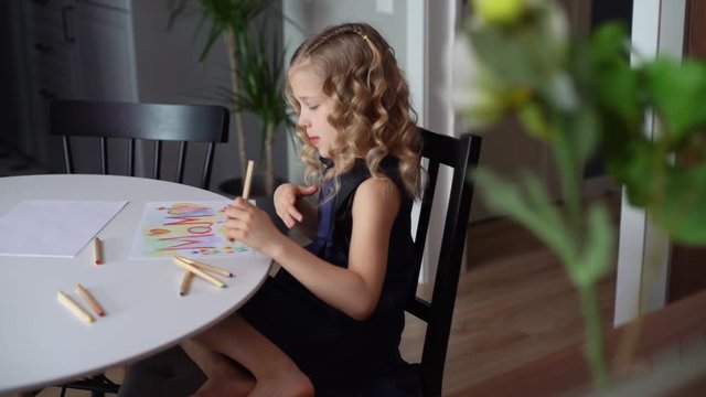 Thoughtful girl thinking about what picture do drawing with colorful pencil at the table. Daughter's making a surprise for her mother. Concept of child creative activity. Tracking shot in slow motion.