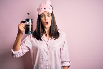 Young brunette woman with blue eyes wearing pajama making coffee with french coffeemaker scared in...