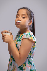 Side view of a girl with milk moustache drinking milk in a glass
