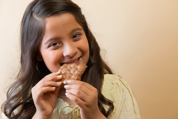 Smiling girl eating a chocolate bar with both hands
