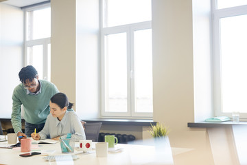 Horizontal shot of young African American man helping his female colleague with work in spacious...