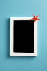 Flatlay red starfish on a blank photo frame on a blue background. The concept of travel, vacation by the sea. Copy space