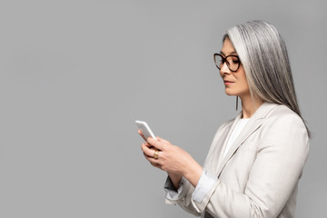 beautiful asian businesswoman in eyeglasses with grey hair talking on smartphone isolated on grey