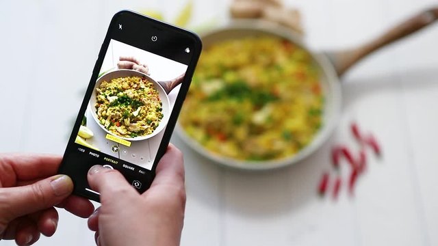 Woman taking a photos with mobile phone of delicious fried rice with chicken served in pan
