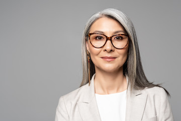 attractive smiling asian businesswoman in eyeglasses isolated on grey