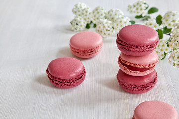 Pink macarons / macaroon on a white wooden table with tender white blossoms in the background.