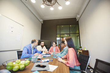 Group of stylish office workers sitting together in modern office board room doing brainstorming, copy space