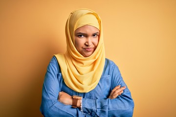 Young beautiful woman with curly hair wearing arab traditional hijab over yellow background skeptic...