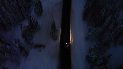 Aerial shot of car driving on curvy road in snowy landscape at night