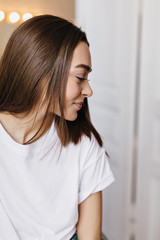 Indoor portrait of pleasant girl with brown shiny hair. Shy smiling woman posing at home in weekend.