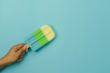 Table top view aerial image of sign or food of summer season holiday background concept.Flat lay of Man hand holding sweet pastel ice cream on modern rustic blue sea paper backdrop.Minimalism design.