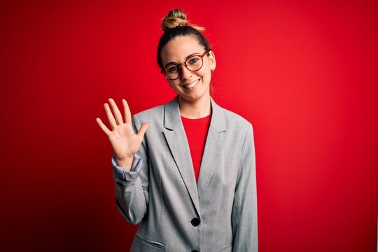 Young beautiful blonde businesswoman with blue eyes wearing glasses and jacket showing and pointing up with fingers number five while smiling confident and happy.