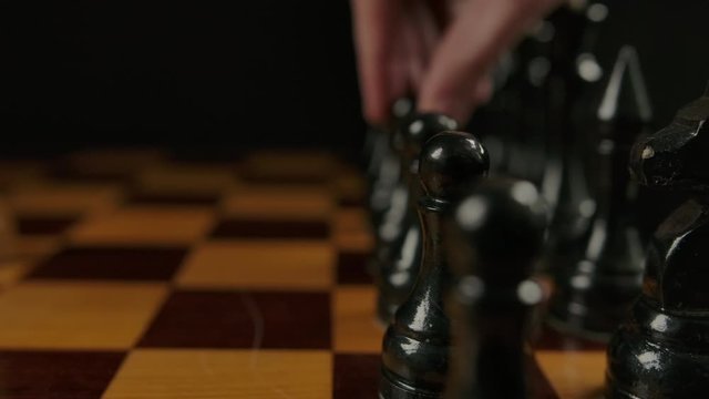 Human's hand makes first opponent move by black pawn e7 e5 in chess game. Macro parallel dolly shot of wooden authentic chess. Two players gaming.