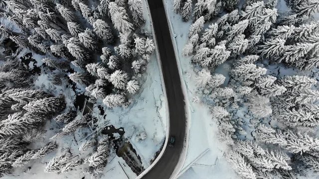 Aerial shot from above of a lonely car driving through snowy landscape on small curvy road in the Italian alps 