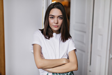 Confident lady with straight hairstyle standing in her apartment with arms crossed. Indoor shot of...