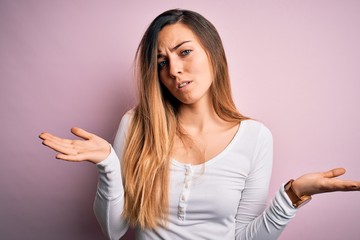 Young beautiful blonde woman with blue eyes wearing white t-shirt over pink background clueless and...