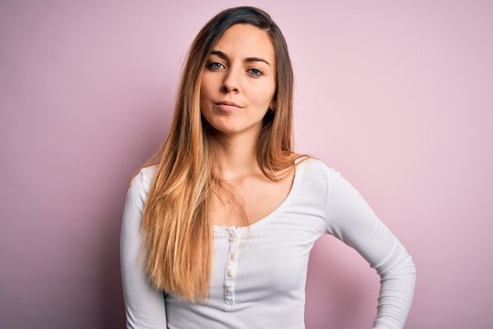 Young beautiful blonde woman with blue eyes wearing white t-shirt over pink background Relaxed with serious expression on face. Simple and natural looking at the camera.