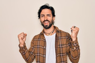 Young handsome hispanic bohemian man wearing hippie style standing over isolated background celebrating surprised and amazed for success with arms raised and open eyes. Winner concept.