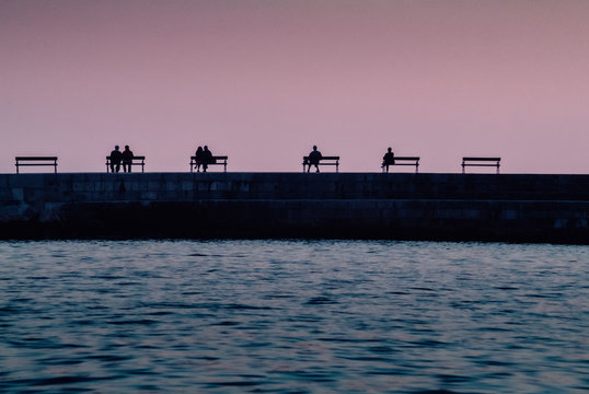 5 B&auml;nke im rosa Abendlicht mit Paare und einzelen Personen am Hafen von Dubrovnik, Kroatien