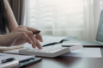 Close up Business woman using calculator and laptop for do math finance on wooden desk in office and business working background, tax, accounting, statistics and analytic research concept