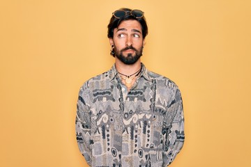 Young handsome hispanic bohemian man wearing hippie style and sunglasses smiling looking to the side and staring away thinking.