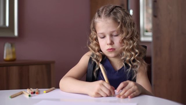 Portrait of cute curly girl thinking about what picture do drawing with colorful pencil at the table in cozy children's room. Concept of child creative activity. Shooting in slow motion.