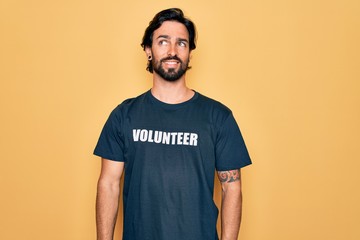 Young handsome hispanic volunteer man wearing volunteering t-shirt as social care smiling looking...