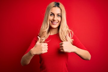 Young beautiful blonde woman wearing casual t-shirt standing over isolated red background success sign doing positive gesture with hand, thumbs up smiling and happy. Cheerful expression.