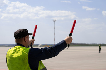 An airport marshal in a yellow uniform helps signals to park by plane. The supervisor meets a...