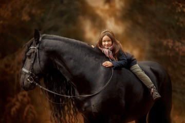 Obraz premium Little girl with Friesian stallion with long hair outdoor portrait in an autumn forest