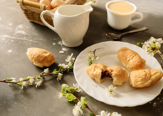 Croissants and coffee with milk on a black background with flowering branches of cherry
